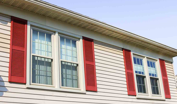 A home with beige siding has new double-hung windows with red shutters.