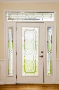 A beautiful front door with white frames and decorative glass with sidelites and a transom.