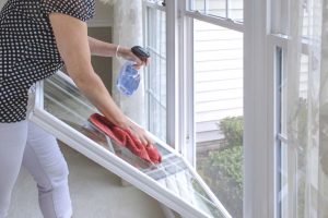 Woman Cleaning her white vinyl double hung tilt in windows.
