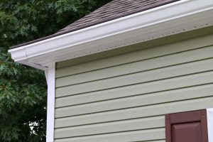 Close up of gutter installed on a house with light green siding and brown asphalt roof