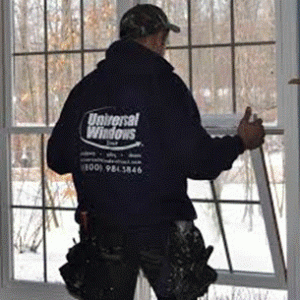 A technician in a sweatshirt installs a replacement window.
