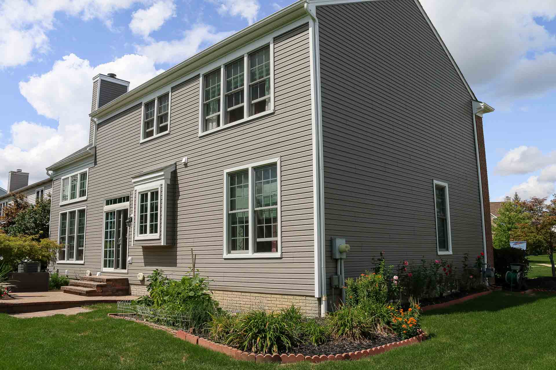 A large home with white-framed windows and new vinyl siding in a gray color.