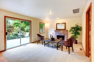 Living room with sitting area by the fireplace with wicker chairs and coffee table. Room decorated with candles and palm tree.