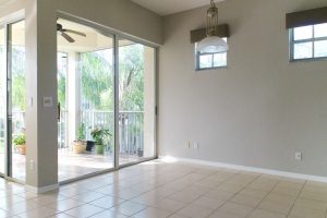 View of an empty neutral colored room with high windows and sliding glass doors to balcony
