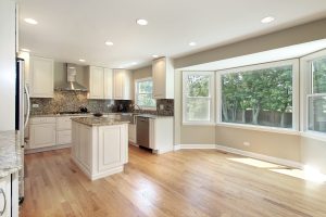 Open kitchen with wood floors and large bay windows.