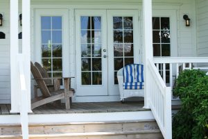 The back porch of a luxury home with Adirondack chairs and wicker furniture.